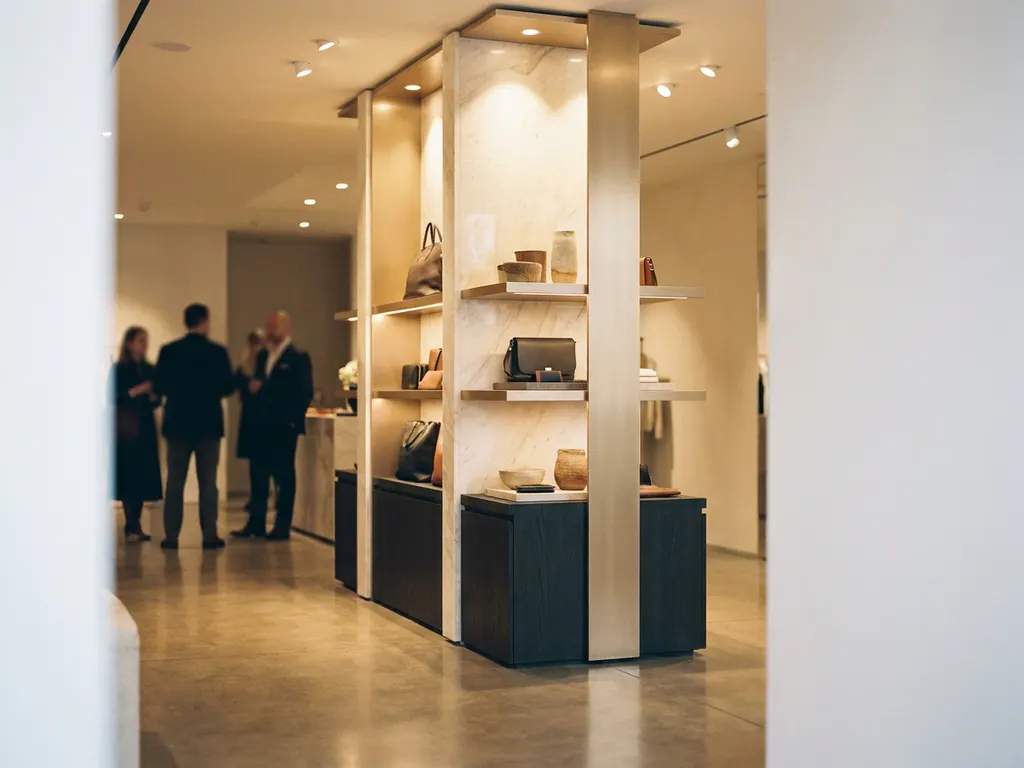 Floor-standing display unit in a high-end retail interior with warm spotlights, cream tones, and polished shelving surfaces.